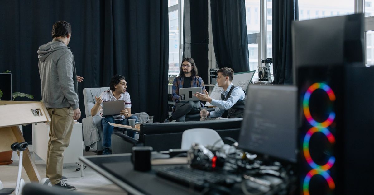 A group of professionals engaged in a casual meeting at a modern office, discussing projects on laptops and tablets.