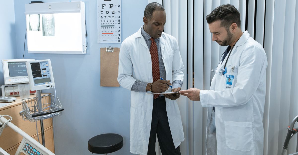 Two doctors in lab coats discussing a patient's medical chart in a hospital setting.