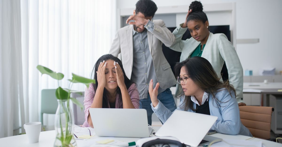 A diverse group of coworkers appearing stressed while working in a modern office meeting room.