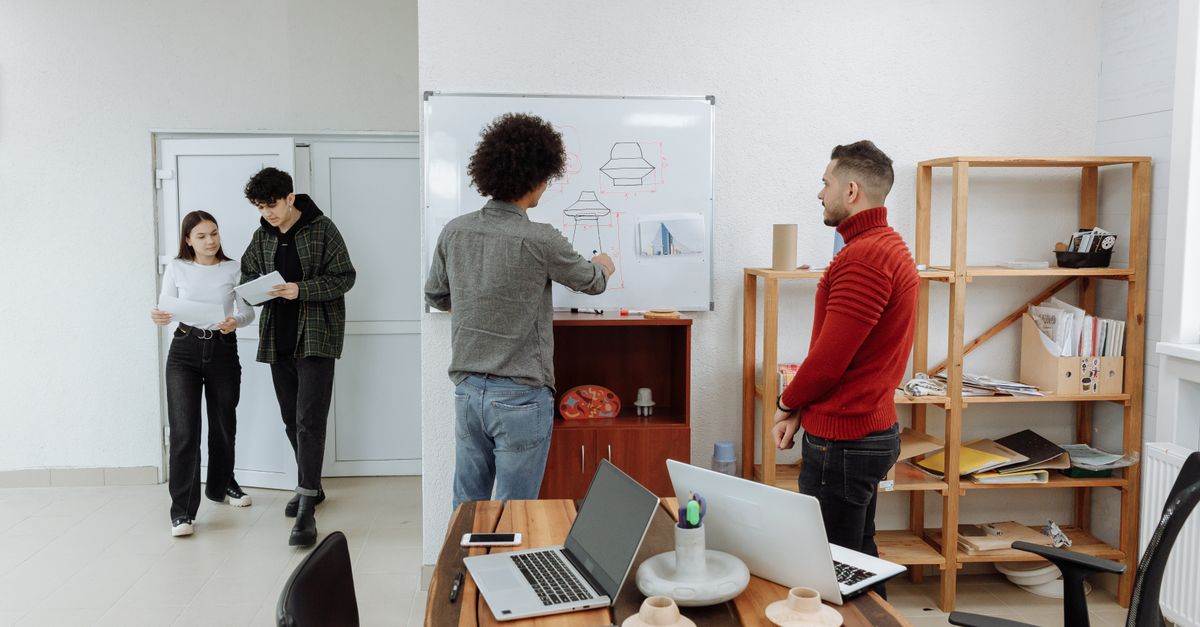 Diverse team collaborating in a modern office, discussing ideas with laptops and a whiteboard.