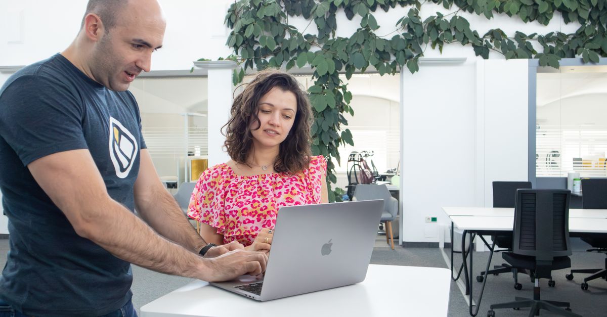 Two colleagues discussing work on a laptop in a bright, modern office environment.