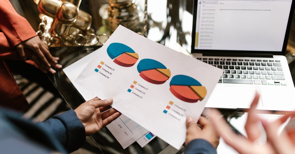 Professional hands holding pie chart data near laptop in modern office setting.
